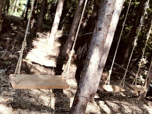 A wooden swing suspended by ropes in a forested area.