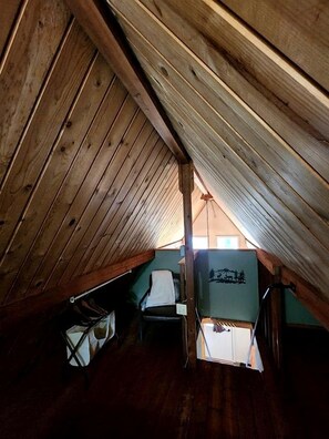 A small attic room with wooden beams, a chair, and a table.