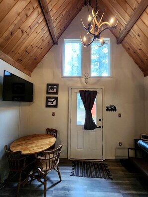A wooden interior with a dining table and chairs, a chandelier, a door with curtains, and a mounted television. - Fantastic Cabin Next to Wonderful Hiking Trails in Seward, Alaska (Seward)