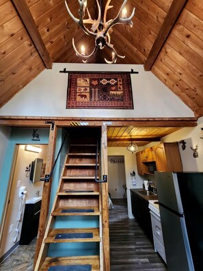 A wooden staircase leading to a kitchen with a chandelier and a decorative wall hanging. - Fantastic Cabin Next to Wonderful Hiking Trails in Seward, Alaska (Seward)