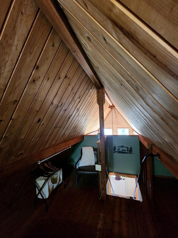 Une petite chambre mansardée avec des lambris en bois au plafond, un lit superposé et une fenêtre donnant sur un beau paysage.