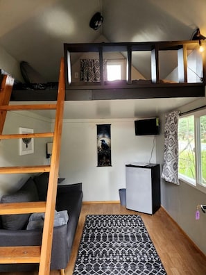 Un cuarto estilo loft con escalera de madera, sofá, escritorio, televisor y alfombra estampada.