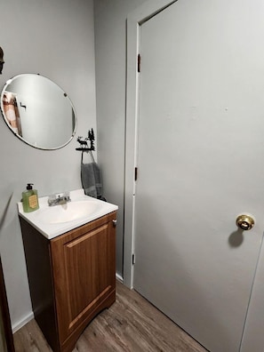 A bathroom with a wooden cabinet, a round mirror, a sink, and a towel rack.