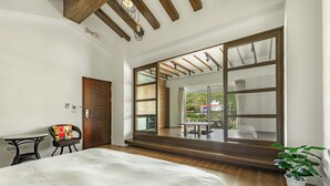 A bedroom with a large window, wooden beams, a bed, a chair, and a small table. - Ghana Inn (Hengchun)