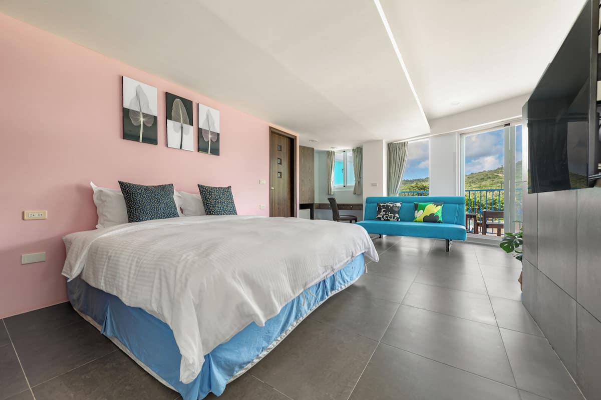 A modern bedroom with a large bed, a blue sofa, and a balcony with a view.