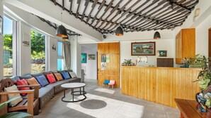 A modern interior with a wooden reception desk, a seating area with colorful cushions, and a large window providing a view of the outdoors. - Ghana Inn (Hengchun)