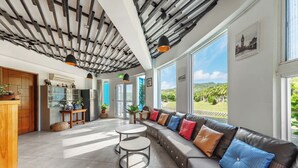 A modern interior with a large seating area, a kitchen, and large windows offering a view of greenery. - Ghana Inn (Hengchun)