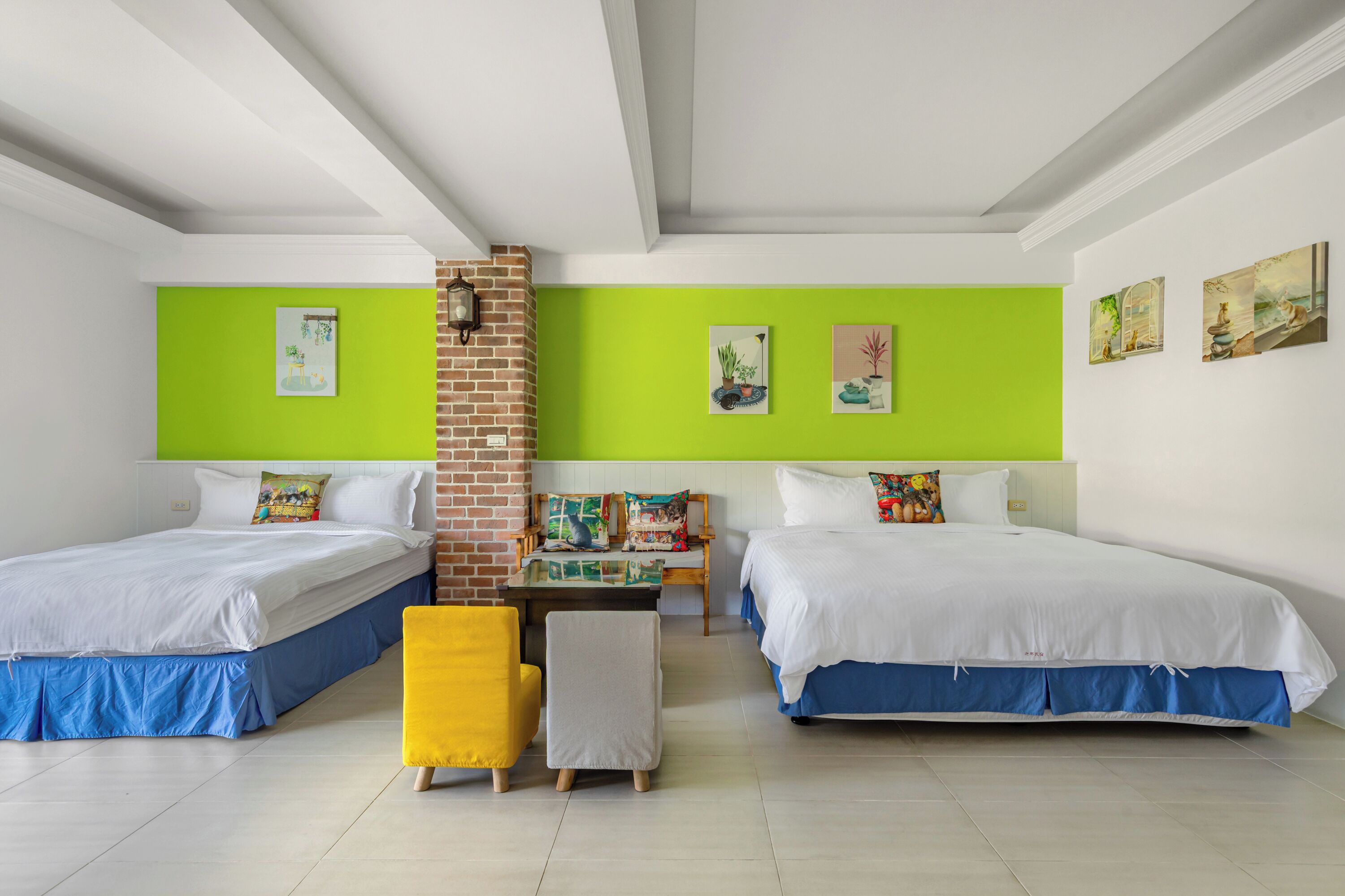 Una habitación de hotel con dos camas, una pared de acento de ladrillo y obras de arte en paredes verdes.