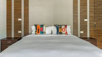 A neatly made bed with a white comforter and two pillows with colorful text. There are wooden panels on the walls and a small wooden nightstand beside the bed.