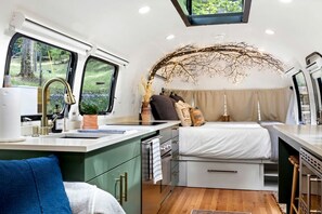 A compact RV interior with a kitchenette, a bed, and a small dining area. - Glamping Getaway in Pisgah Forest in this Lovely Airstream Rental in North Carolina (Pisgah Forest)