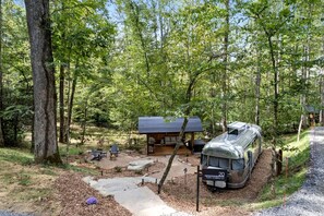 A forested campsite with a covered picnic area, a camper, and a stone path leading to the entrance. - Glamping Getaway in Pisgah Forest in this Lovely Airstream Rental in North Carolina (Pisgah Forest)