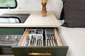 A kitchen drawer with utensils, a window with a view, and a vase with dried plants on the counter. - Glamping Getaway in Pisgah Forest in this Lovely Airstream Rental in North Carolina (Pisgah Forest)