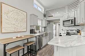 A modern kitchen with a central island, stainless steel appliances, and a large abstract painting. - Beautiful Cabin with Fire Pit and Barbecue in Fredericksburg, Texas (Fredericksburg)