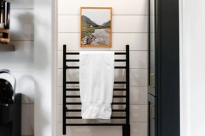 A towel hanging on a black towel rack in a bathroom with a picture of a landscape on the wall.