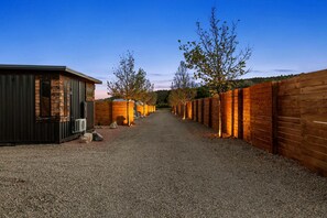 Ein Kiesweg führt zu einer Reihe von Ferienhäusern, an einer Seite eine Holzlattenverkleidung und auf der anderen ein Metallgebäude.