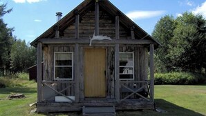 A rustic wooden cabin with a gabled roof, a central door, and two windows on the side. - Rustic, Private Log Cabin near Augusta, Maine, Perfect for a Weekend Getaway in Nature (Pleasant Ridge Plantation)