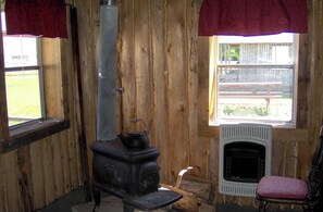 En rustik stuga med en vedeldad kamin, en öppen spis, ett fönster med utsikt och en stol.