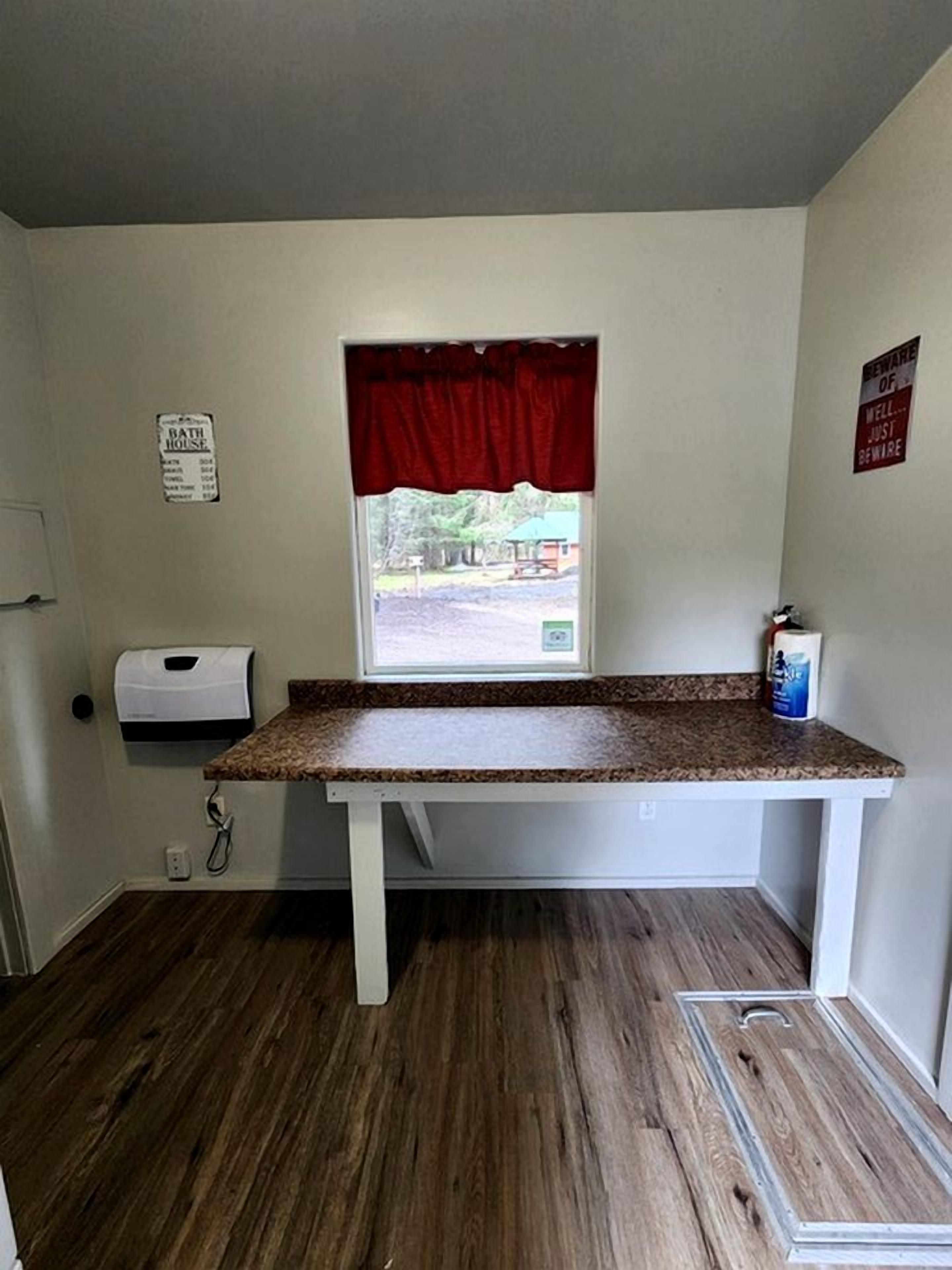 A bathroom with a window, a red curtain, a sign on the wall, and a countertop.