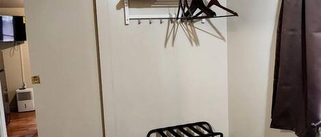 A bedroom with a bed, a hanging laundry rack, a coat rack, and a television.