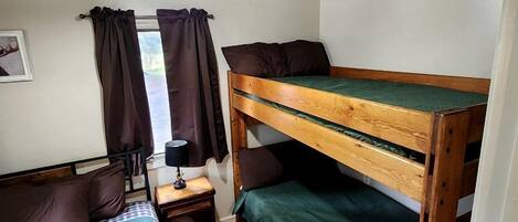 A compact room with bunk beds, a small table with a lamp, and a window with curtains.