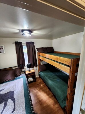 Une pièce de taille modeste, avec des lits superposés, une petite table avec une lampe et une fenêtre avec des rideaux.