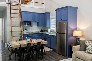 A compact kitchen with blue cabinets, a stainless steel refrigerator, a wooden dining table with chairs, and a ladder. - Outstanding Cabin Incredible for Six People in Livingston, Texas (Livingston)