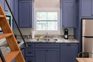 A kitchen with blue cabinets, a stainless steel refrigerator, a window with blinds, and a coffee maker on the counter. - Outstanding Cabin Incredible for Six People in Livingston, Texas (Livingston)