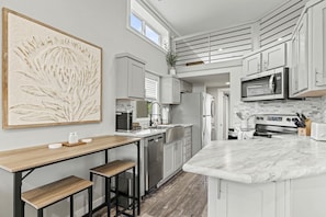 A modern kitchen with a central island, stainless steel appliances, and a large abstract painting. - Pet-Friendly Cabin with Lofted Interior and Water Views in Texas (Fredericksburg)