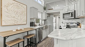 A modern kitchen with a central island, stainless steel appliances, and a large abstract painting. - Pet-Friendly Cabin with Lofted Interior and Water Views in Texas (Fredericksburg)