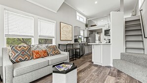 A modern living room with a grey sofa, a coffee table, and a kitchen in the background. - Pet-Friendly Cabin with Lofted Interior and Water Views in Texas (Fredericksburg)