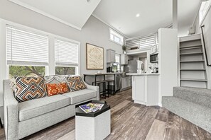 Ein modernes Wohnzimmer mit grauem Sofa, einem Couchtisch und einer Küche im Hintergrund.