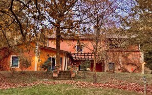 A rustic building with a red facade, a covered porch, and a garden area with a stone bench. - Relaxing Retreat With Personalized Chef Cooking Class & Relaxation Services (San Casciano dei Bagni)