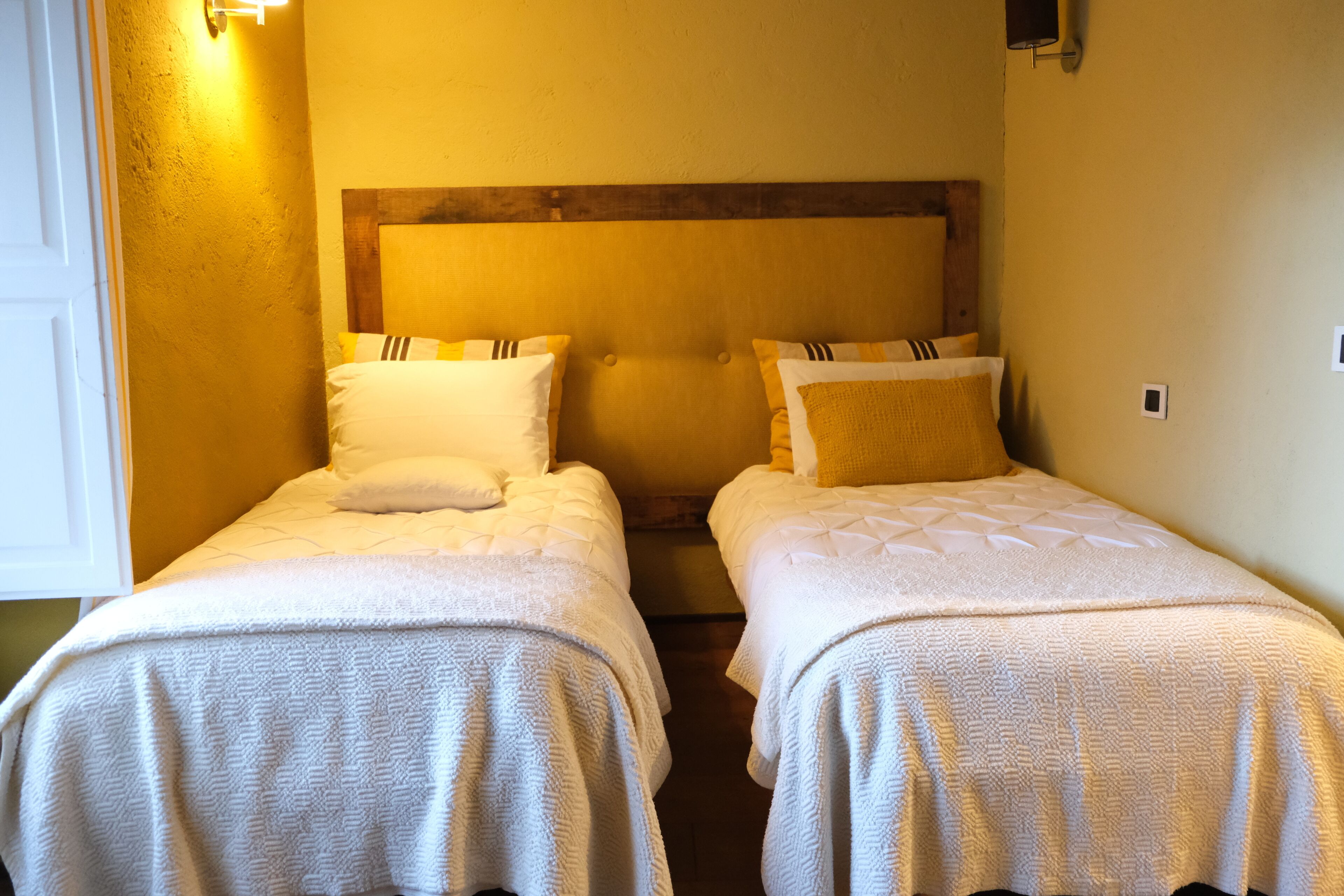 A room with two single beds, each with a wooden headboard and white bedding.