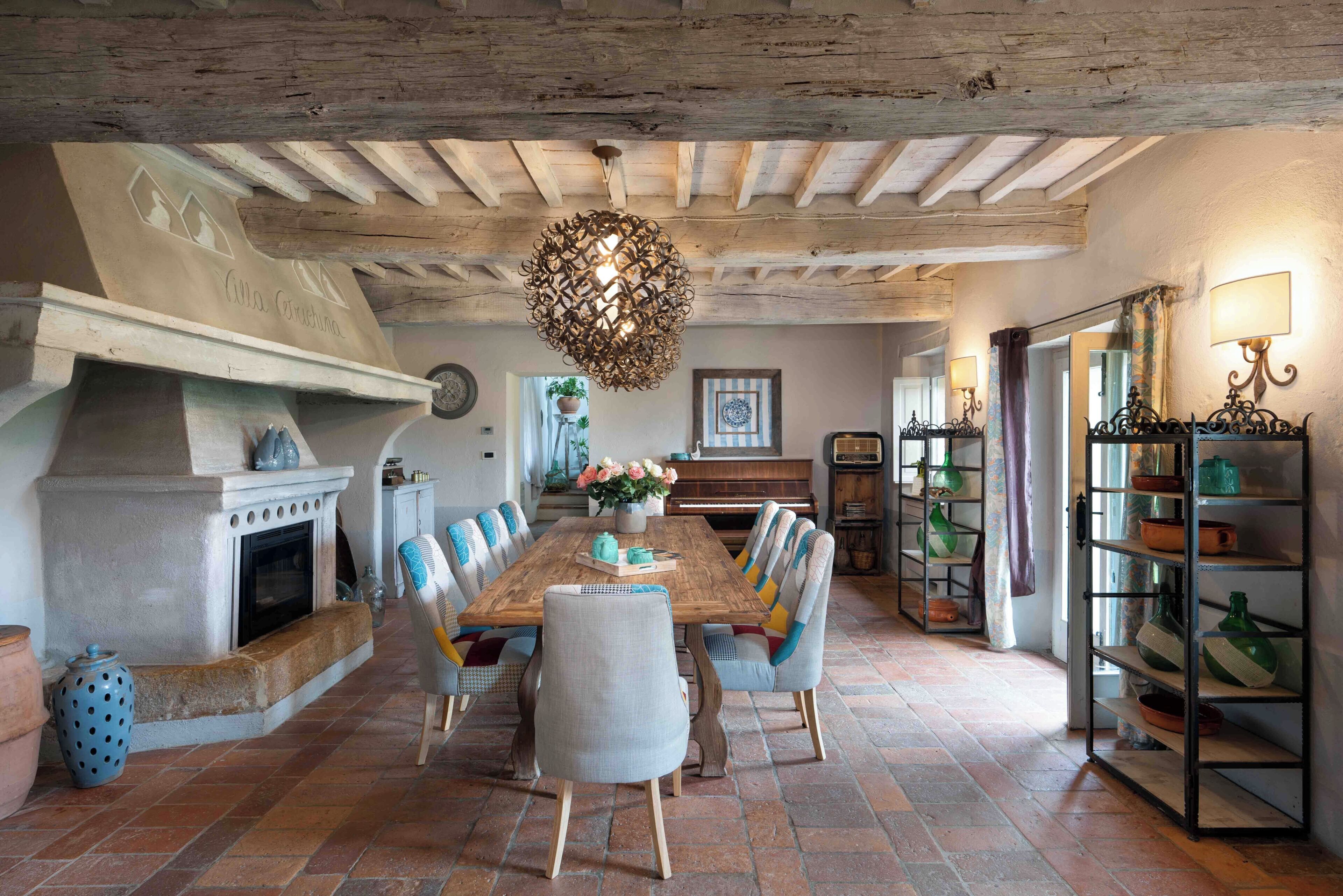 A dining area with a large wooden table, chairs, a fireplace, and a hanging light fixture.