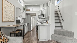 Una cocina compacta con armarios blancos, una zona de comedor con un banco y una escalera.