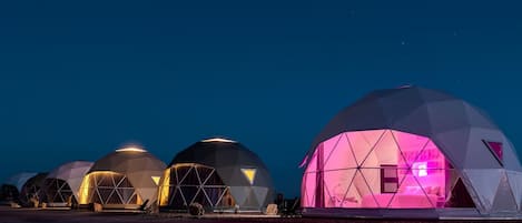 A series of geodesic dome structures with interior lighting, likely accommodations, set against a night sky.
