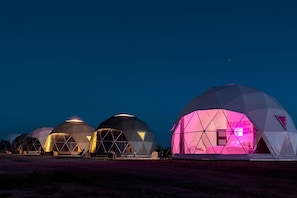 A series of geodesic dome structures with interior lighting, likely accommodations, set against a night sky.