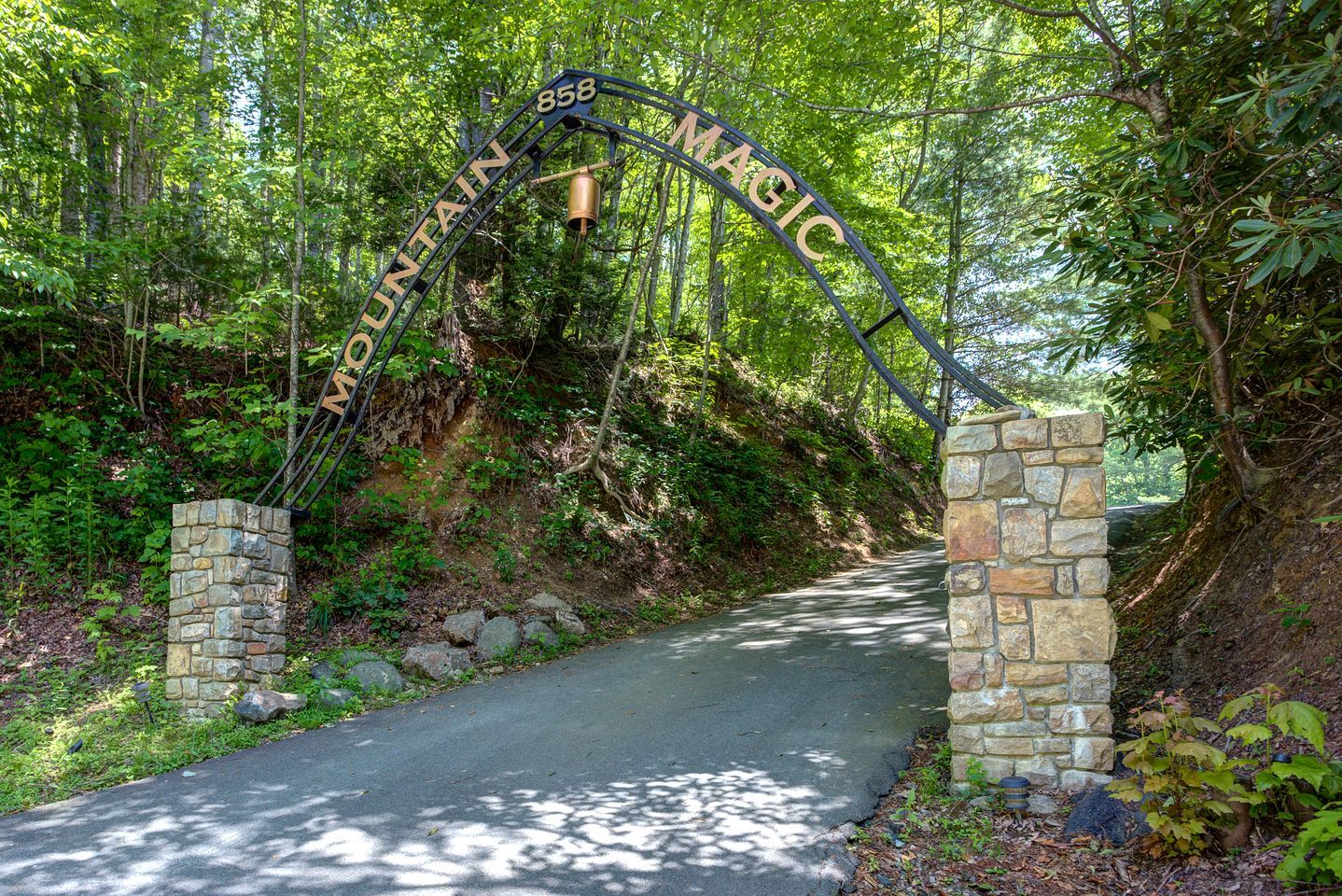 A stone archway with 'MOUNTAIN MAGIC' written on it, leading to a paved path surrounded by trees.
