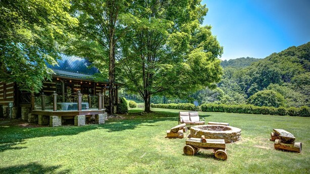 Un chalet rustique doté d’une cheminée en pierre, d’un espace extérieur aménagé et offrant une vue sur une forêt luxuriante.