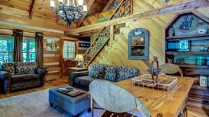 L’intérieur d’une cabane avec un escalier en bois, un lustre, un canapé, une table à manger et une bibliothèque.