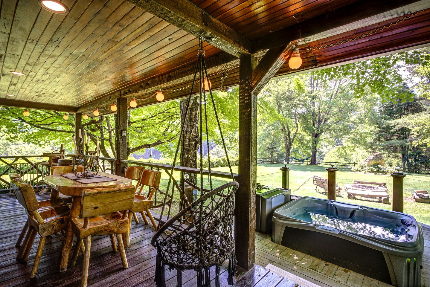 A wooden deck with a table and chairs, a hot tub, and a view of a wooded area.