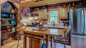 Une cuisine rustique avec des meubles de rangement en bois, un réfrigérateur en acier inoxydable et une table à manger en bois, accompagnée de chaises.