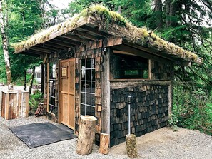 Une cabane rustique avec un toit de chaume, des murs en bois et un petit espace porche.