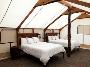 Une tente équipée de deux lits, avec des poutres en bois et un aménagement simple et fonctionnel.
