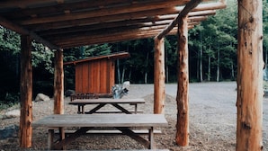 A rustic wooden structure with a picnic table and a small cabin-like building.