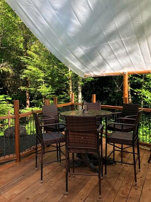 Une terrasse en bois avec une table et des chaises, entourée d’un auvent blanc.