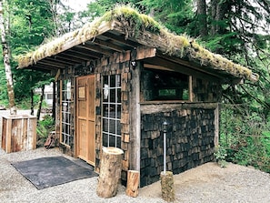 A rustic cabin with a thatched roof, wooden walls, and a small porch area. - Rustic and Spacious Safari Tent in Forks, Washington, Perfect for a Glamping Getaway to the Pacific Northwest (Forks)