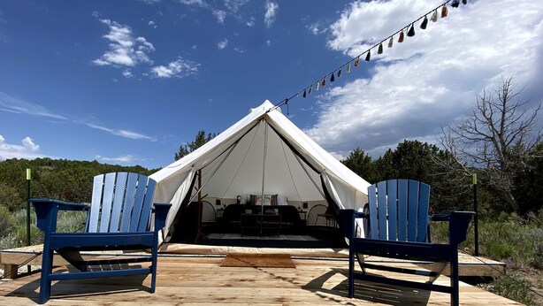 A tent with a wooden deck, two blue Adirondack chairs, and a string of colorful flags.