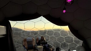 Una stanza con un letto grande, una sedia e vista attraverso una finestra esagonale.