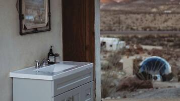 A bathroom with a white sink, a mirror, and a view of a desert landscape.
